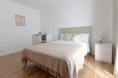 Dormitorio luminoso en Apartamentos El Sol II Tossa de Mar con cama queen, mesita de noche blanca, cocineta y suelos de madera
