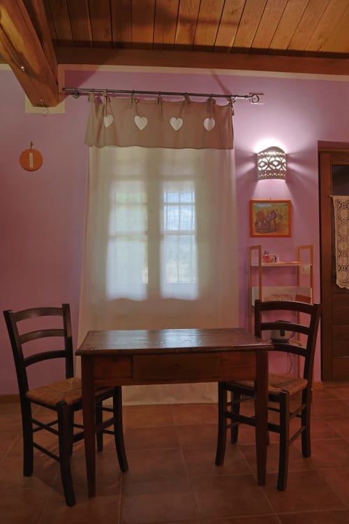 Accogliente camera rosa a La Casa dei Tigli B&B a Cannara con tavolo in legno, sedie e tende trasparenti che incorniciano la vista del giardino