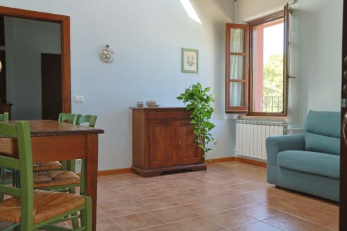 Luminoso soggiorno della Casa dei Tigli a Cannara con sedie verdi, arredamento in legno, divano blu e vista sul giardino