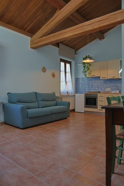 Appartamento Azzurro a La Casa dei Tigli a Cannara, Italia. Soggiorno moderno con divano blu, cucina, travi in legno e