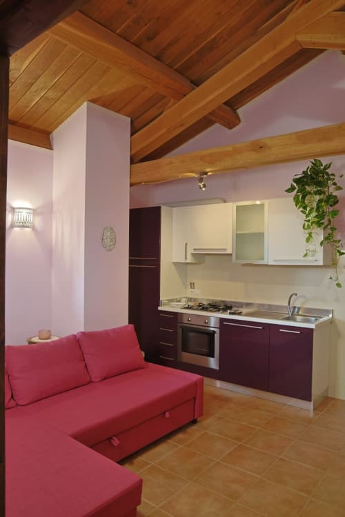 Appartamento Rosa a La Casa dei Tigli con pareti rosa, travi in legno, divano rosso e cucina moderna a Cannara