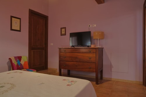 Camera da letto Malva presso La Casa dei Tigli a Cannara con pareti rosa, cassettone in legno, TV e biancheria floreale