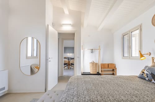 Luminosa camera moderna a Case Luparello con letto grigio, specchio rotondo, arredi in legno e finestre con vista sul giardino