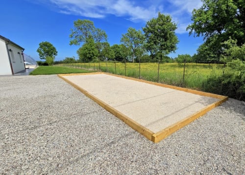 Terrain de pétanque du gîte Vindihouses à Magnien avec pelouse entretenue et arbres au-delà de la clôture