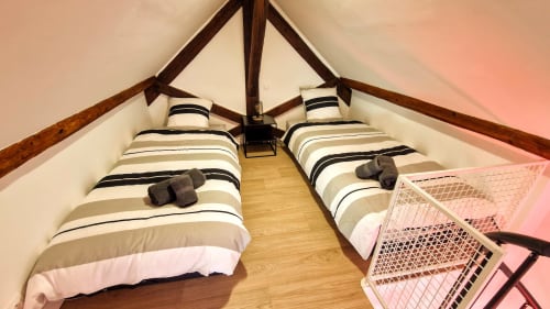 Twin beds in loft bedroom at Vindihouses cottage, Épinac. Striped bedding with exposed wooden beams.