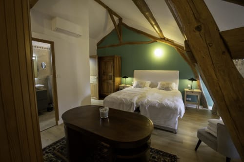 Chambre spacieuse au gîte Domaine Chapelle avec mur d'accent vert, lit blanc, poutres apparentes et coin salon