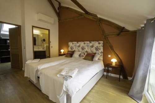 Chambre spacieuse à la Domaine Chapelle B&B avec lits jumeaux, tête de lit fleurie, murs marron chaud et vue sur le jardin