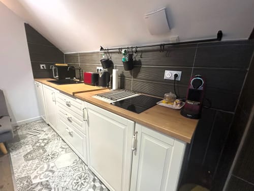 Kitchenette moderne au Domaine Chapelle avec armoires blanches, plan de travail bois, crédence noire et cafetière