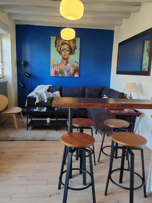 Espace commun moderne à la Domaine Chapelle B&B avec mur d'accent bleu, canapé noir, tabourets de bar en bois et portrait pop art