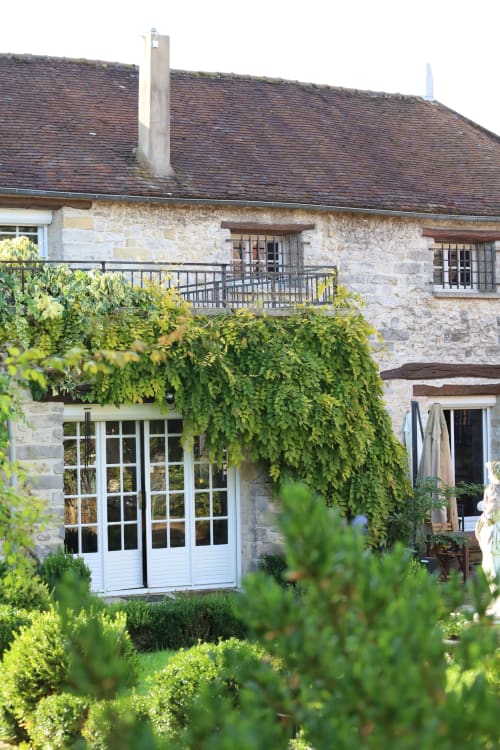 Chaumière de pierre au Domaine Chapelle aux murs couverts de lierre, portes blanches, terrasse supérieure et jardin luxuriant à La Chapelle-la-Reine