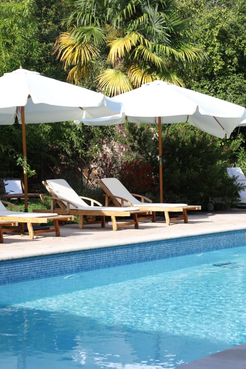 Piscine aux carrelages bleus, transats en bois sous parasols blancs, jardin luxuriant en arrière-plan à Domaine Chapelle