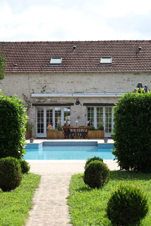 Vue de la piscine du Domaine Chapelle avec maison en pierre, piscine bleue, jardins paysagés et coin détente