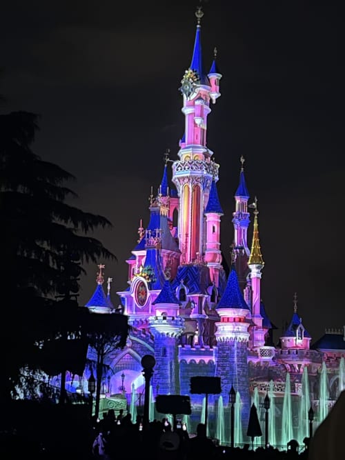 Château enchanté illuminé de rose et bleu la nuit près de Cramoisy