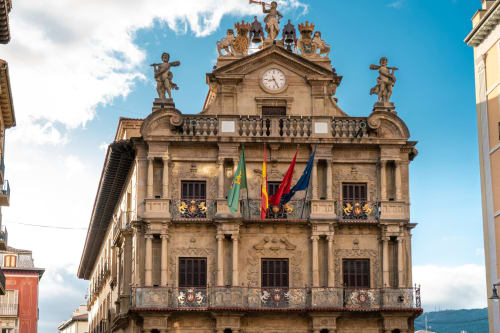 Edificio histórico de piedra con torre reloj, estatuas decorativas y banderas españolas en Hostal Iruña Rooms, España