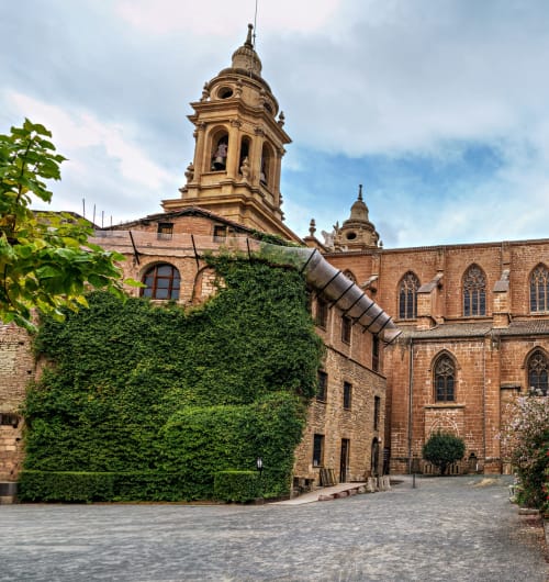 Patio histórico de catedral de ladrillo con muro cubierto de hiedra y campanario, Hostal Iruña Rooms, España