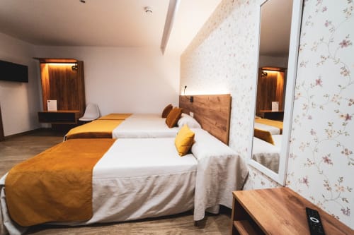Habitación triple del Hostal Restaurante Angel en Huelma con camas gemelas, cabeceros de madera, detalles amarillos y papel tapiz floral