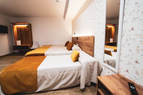 Habitación triple en Hostal Restaurante Angel de Huelma con dos camas, cabeceros de madera, detalles en amarillo y comodidades modernas