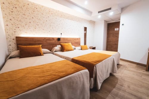 Habitación triple en Hostal Restaurante Angel en Huelma con dos camas, detalles en naranja, cabecero de madera y comodidades modernas