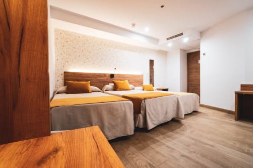 Habitación triple del Hostal Restaurante Angel en Huelva con dos camas, cabecero de madera, detalles en amarillo y mobiliario moderno