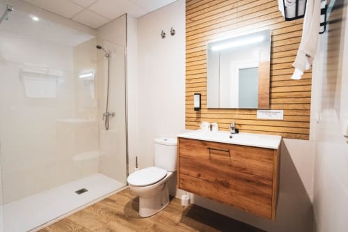 Baño moderno del Hostal Restaurante Angel con tocador de madera, ducha amplia, inodoro y espejo iluminado