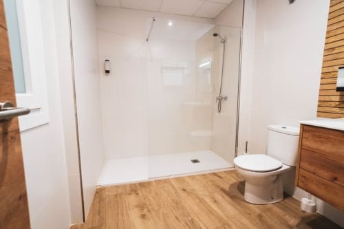 Baño moderno en Hostal Restaurante Angel de Huelma con ducha de obra, azulejos blancos, piso de madera, inodoro y lavamanos.