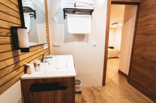 Baño moderno en Habitación Triple del Hostal Restaurante Angel, Huelma, con detalles de madera, lavabo blanco, espejo y toalla