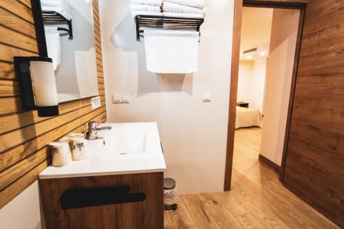 Baño moderno del Hostal Restaurante Angel con mueble de madera, lavabo blanco, espejo, toalleros y piso de azulejos