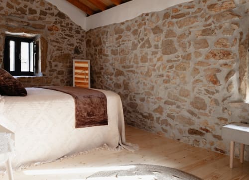 Quarto rústico de pedra em Recantos D'Almerinda em Pombal com paredes de tijolos aparentes, pisos de madeira e roupas de cama creme