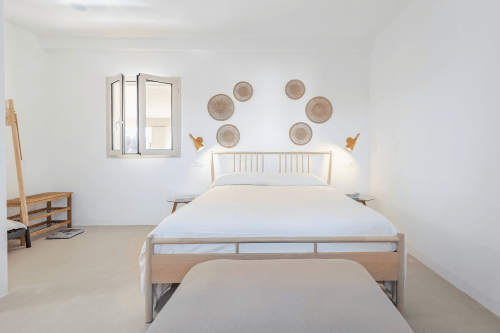 Camera luminosa a Case Luparello con letto in legno, piatti tessuti in parete e luce naturale nell'appartamento di Noto