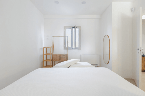 Camera da letto minimalista a Case Luparello a Noto con biancheria bianca, elementi in legno e vista sul giardino