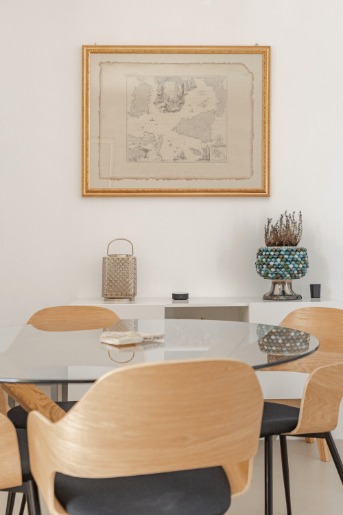 Zona pranzo moderna a Case Luparello con sedie in legno, tavolo bianco e mappa vintage incorniciata a Noto
