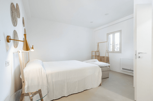 Camera da letto luminosa e minimalista a Case Luparello a Noto con letto bianco, mobili in legno e decorazioni tessili murali