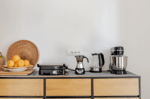 Bancone della cucina con caffettiera, bollitore e cesto di frutta all'appartamento Case Luparello, Noto