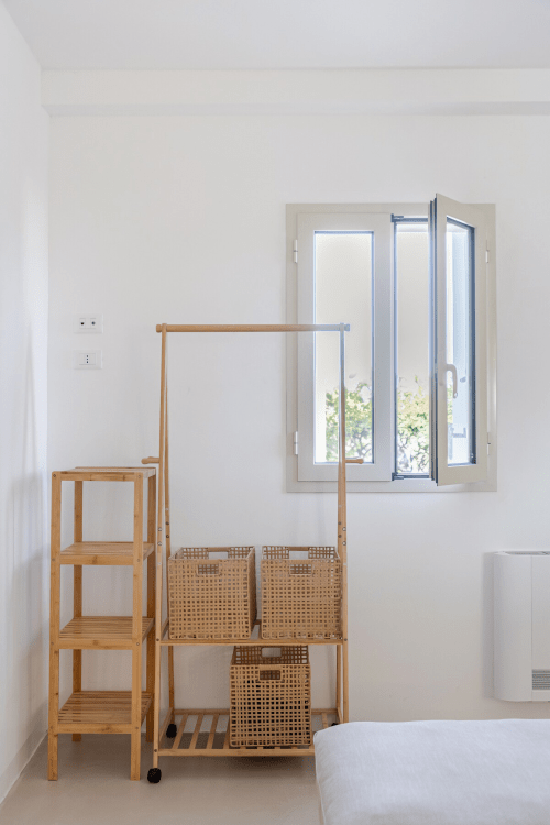 Camera minimalista a Case Luparello con scaffali in legno, cesti intrecciati e porte in vetro che si affacciano sul giardino