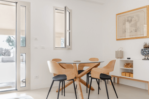 Moderna sala da pranzo nell'appartamento Biancolilla a Case Luparello con sedie in legno, tavolo rotondo in vetro e luminosa vista sul giardino