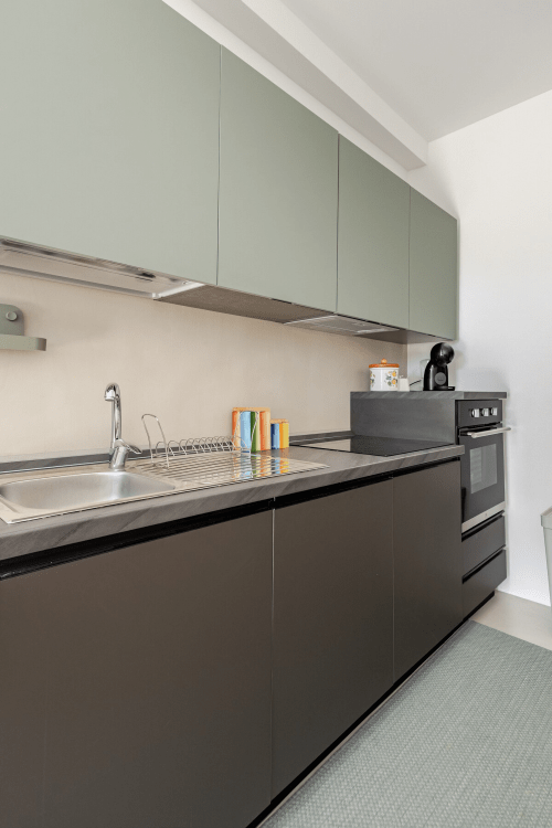 Cucina moderna nell'appartamento Biancolilla di Case Luparello, Noto, con mobili verde salvia e unità inferiori scure