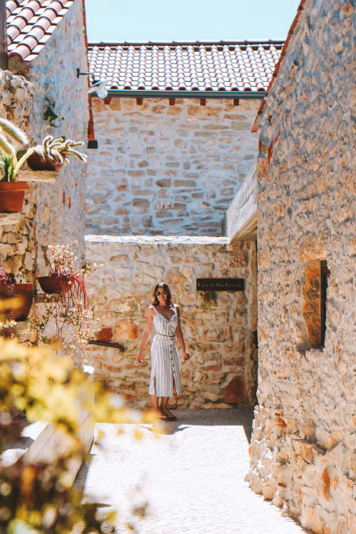 Mulher em vestido branco caminhando pelo pátio de pedra do hotel Recantos D'Almerinda em Pombal, Portugal