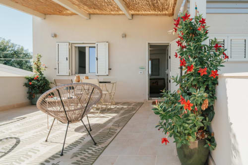 Terrazza soleggiata di Case Luparello a Noto con sedia intrecciata, rampicanti a fiori rossi e patio arredato in stile moderno