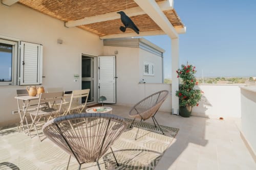 Terrazza dell'appartamento Moresca a Case Luparello, Noto con sedute in vimini, tavolo da pranzo e pianta fiorita sotto cielo sereno
