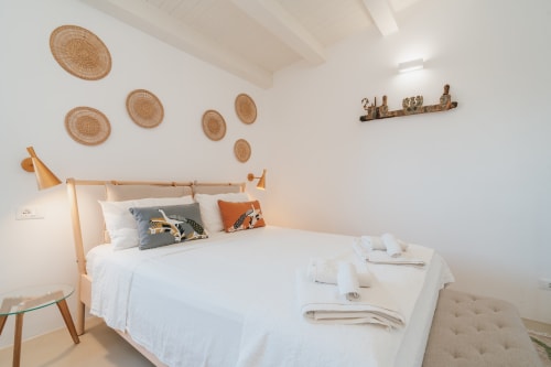 Camera da letto moderna e luminosa a Case Luparello a Noto con letto in legno, cesti tessuti a parete e biancheria bianca