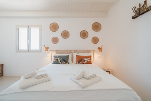 Camera da letto Moresca a Case Luparello, Noto: letto in legno con decori murali intrecciati, biancheria bianca e cuscino arancione
