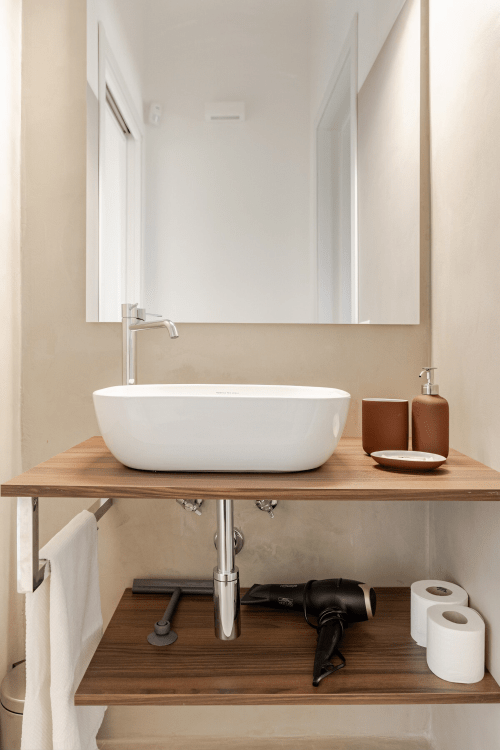 Bagno moderno a Case Luparello con lavabo in ceramica bianca, mobile in legno e ampio specchio nell'appartamento di Noto