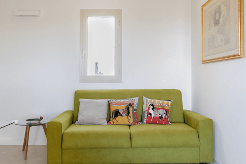 Appartamento Moresca a Case Luparello di Noto con divano verde lime, cuscini decorativi e quadri alle pareti bianche.