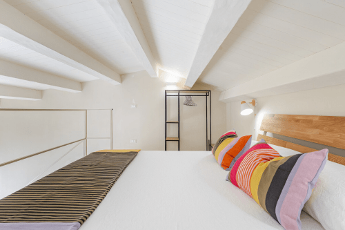 Camera da letto luminosa in soffitta a Case Luparello a Noto, con letto in legno, cuscini colorati e design minimalista