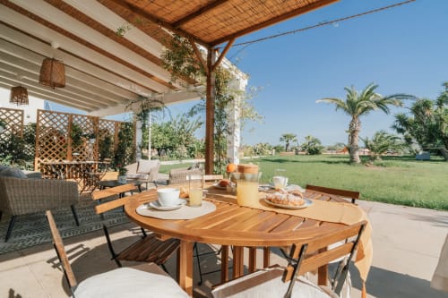 Terrazza dell'appartamento Carolea di Case Luparello a Noto con tavolo in legno, colazione, vista sul giardino e palme