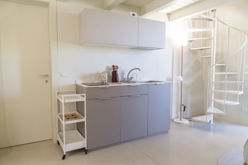 Moderna cucina dell'appartamento Carolea a Case Luparello, Noto: mobili grigio, scaffali bianchi e scala a spirale