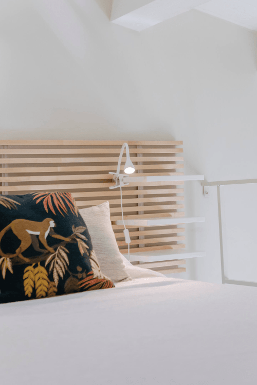 Camera da letto Carolea a Case Luparello con testiera in doghe di legno, cuscini decorativi, biancheria bianca e lampada da lettura