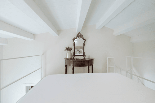 Camera da letto nell'appartamento Carolea a Case Luparello, Noto. Soffitto con travi bianche, toletta d'epoca con specchio ornato e giardino