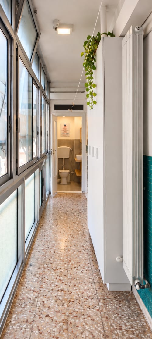 Corridoio luminoso con grandi finestre, pianta sospesa, radiatore bianco e ingresso al bagno condiviso presso Easystay Bari