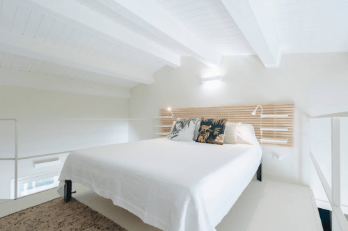 Camera da letto Carolea presso Case Luparello a Noto con testata moderna in legno, biancheria bianca e luminose finestre a soffitto